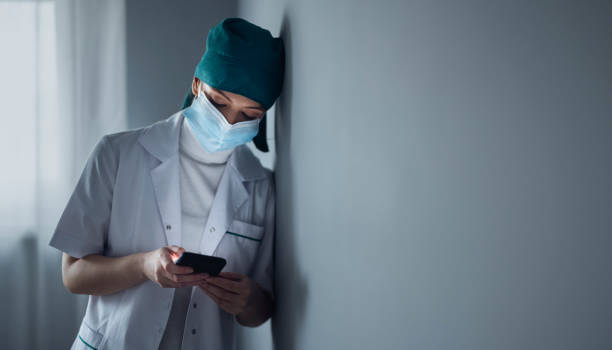 kvinnlig kirurg läser meddelande på mobiltelefonâ i korridoren på sjukhuset - nurse on phone serious bildbanksfoton och bilder