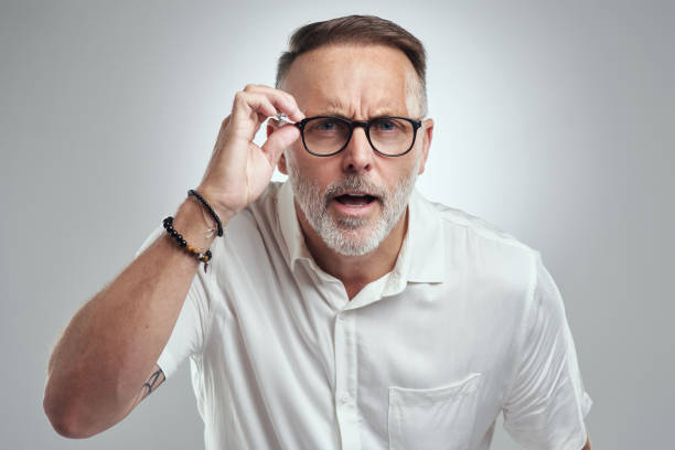 retrato de estudio de un hombre maduro con gafas y mirando confundido sobre un fondo gris - entrecerrar los ojos fotografías e imágenes de stock