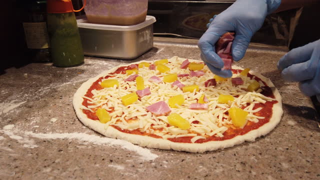 Toppings going onto a Hawaiian pizza