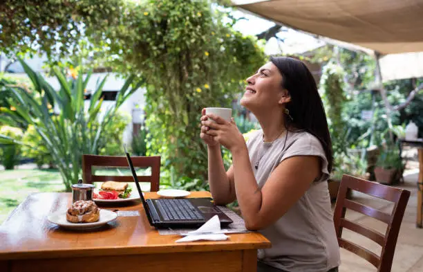Smiling young woman wearing laptop in outdoor cafeteria