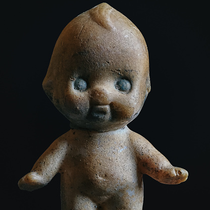 Macro photo of a vintage plastic baby doll that is badly damaged from being left outside in the elements for years; creepy Halloween theme