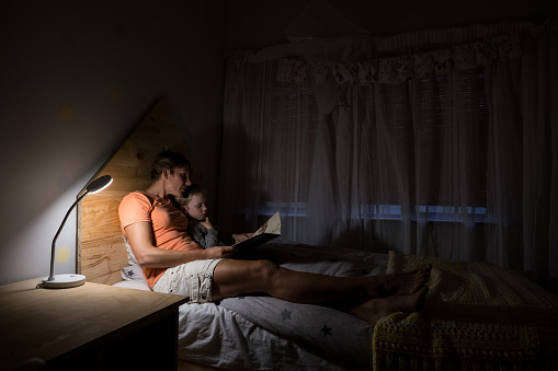 A mother reads a bedtime story to her daughter in her bed at night.