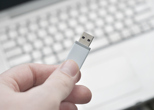 Closeup of a man's hand holding a flash drive above a laptop computer.
