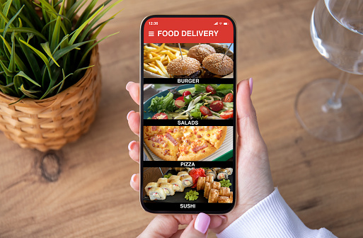 female hands holding phone with food delivery app on screen over wooden table