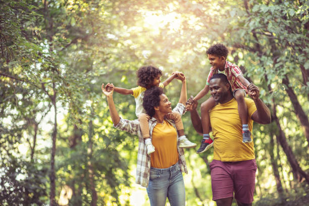 アフリカ系アメリカ人の家族がトラフパークを歩いています。子どもをピギーバックに乗せた親。 - father son ethnic child ストックフォトと画像