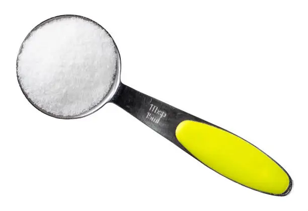 top view of finely ground sea salt in measuring tablespoon cutout on white background