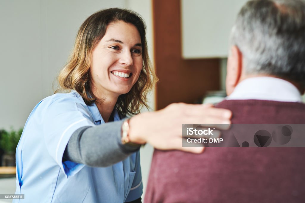 Shot of an attractive young nurse sitting and bonding with her senior patient in his kitchen at home You have nothing to worry about anymore Nurse Stock Photo