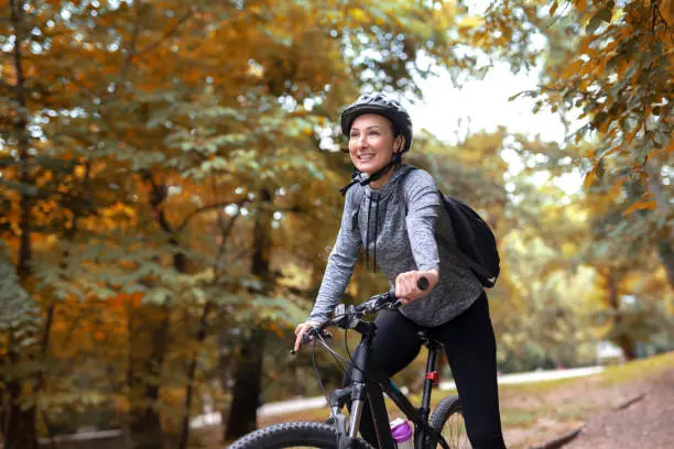 Photo of Young and happy woman in a tracksuit on a mountain bike enjoys in day ride through the park