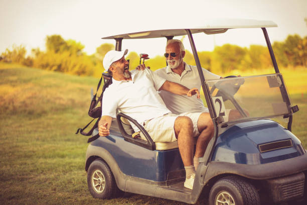 dois amigos mais velhos estão andando em um carrinho de golfe. - senior couple golf retirement action - fotografias e filmes do acervo