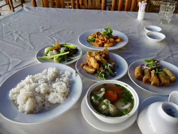 Table setting in a Vietnamese restaurant with small dishes of local food like lumpia, rice, soup and vegetables.