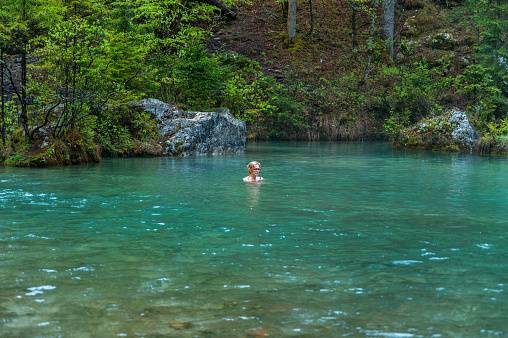 Senior woman standing in a cold river and meditating.