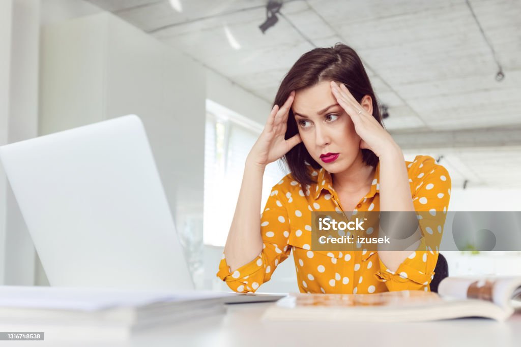 Woman working in the office Tired mid adult women wearing yellow polka dot shirt using computer in the modern white office, looking tired. 30-39 Years Stock Photo