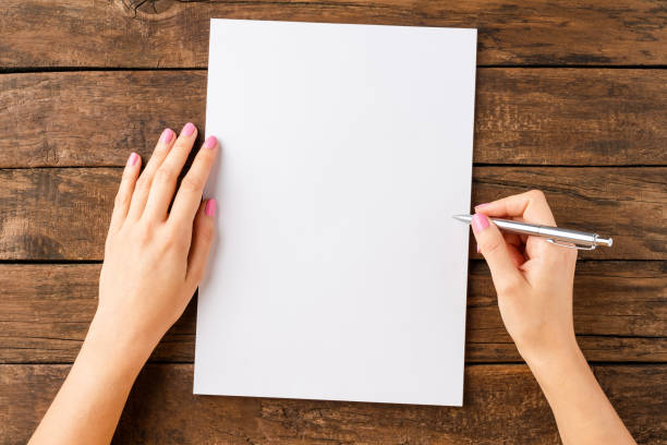 istock Woman’s hands writing with pen over blank white paper sheet on wooden table. Top view 1316750118
