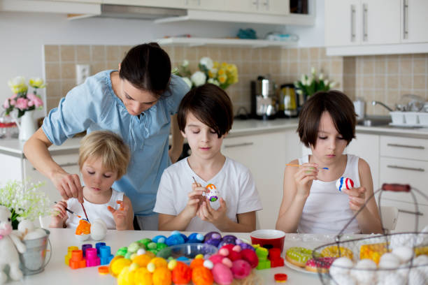 istock Three children, sibling brothers, painting easter eggs for decoration, mom helping them 1316751525