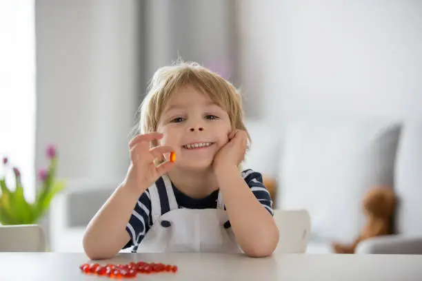 Photo of Cute little child, toddler boy, eating alfa omega 3 child supplement vitamin pills at home