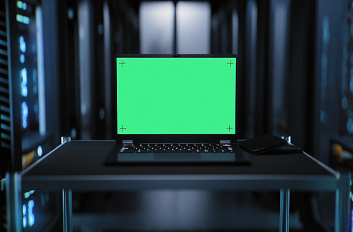 Close-up of a laptop inside a large hallway with supercomputers in a server room data center. Technology used for cloud computing and network security. With chroma key green screen.