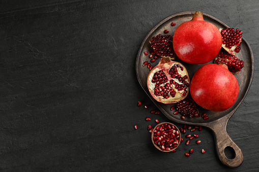 Delicious ripe pomegranates on black table, flat lay. Space for text