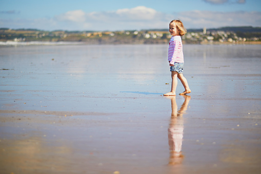 Adorable toddler girl on the sand beach at Atlantic coast of Brittany, France. Small child enjoying vacation by the sea or ocean. Travelling with kids
