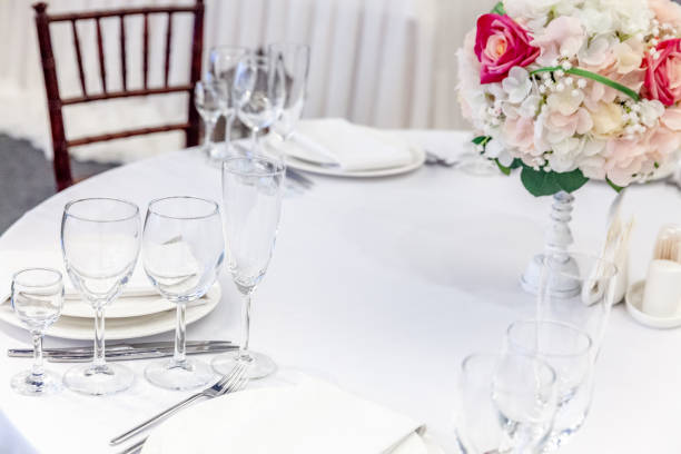 istock Fancy table set for dinner with flower composition in restaurant, luxury interior background. Wedding elegant banquet decoration and items for food arranged by catering service on white table 1316761948