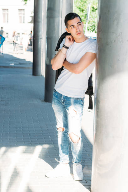 istock young, handsome guy in a white T-shirt, black, leather jacket and blue, torn jeans is on the street, model, city walk, live style. in white sneakers 1316761950