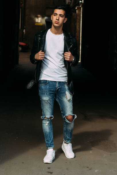 istock young, handsome guy in a white T-shirt, black, leather jacket and blue, torn jeans is on the street, model, city walk, live style. in white sneakers 1316762636