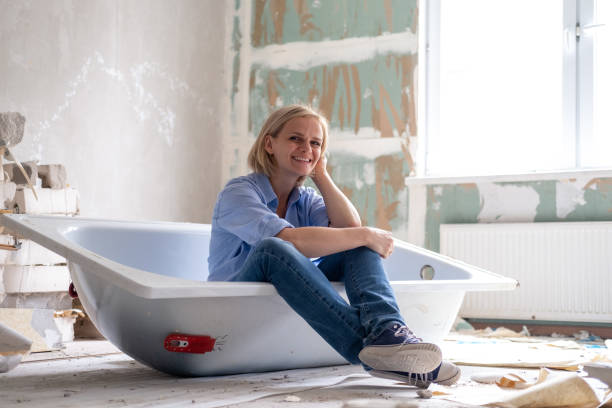 Renovation apartment. Creative story young happy woman sits in bathtub in the middle of the room. Empty walls, repairs house with their own hands stock photo