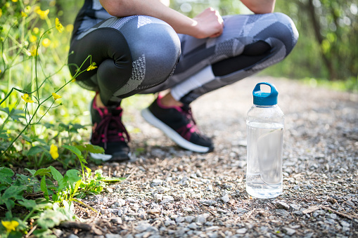 A shot of an unrecognizable woman taking a rest after work out in the front of the picture is a  sustainable bottle fill with water.