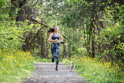A shot of a young woman jogging in the park with her little cute dog.