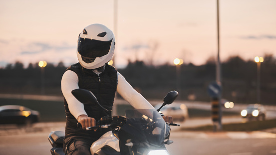Portrait of an young man sitting on motorcycle and wearing a leather jacket and helmet. Night time. Low light. Traffic jam.