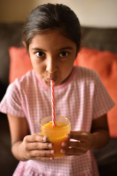 istock Girl drinking Mango juice with straw from her glass sitting on a sofa 1316774406
