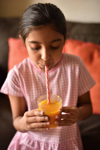 istock Girl drinking Mango juice with straw from her glass sitting on a sofa 1316774411