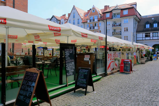Kolobrzeg, Poland - June 23, 2016: Temporary cafes and restaurants covered with a square umbrellas open for the summer season are located on the square in front of town hall. The city of Kolobrzeg, situated on the Baltic coast, is both a town and a health resort. The proximity of the sea makes this resort a popular holiday destination, especially during the summer. The city also serves as a port, there is a commercial port as well as a fishing port. Kolobrzeg is an attractive city for domestic tourists as well as foreigners.