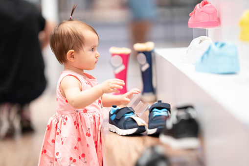 Little cute girl is choosing new shoes. She is looking at the shoes in the shoe shop.