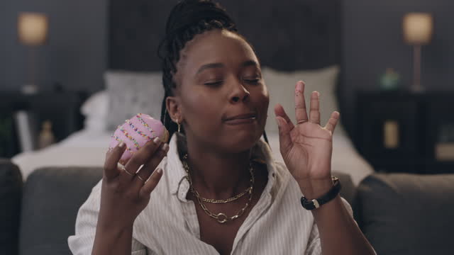 4k video footage of a young woman eating a cupcake while sitting in the bedroom of her apartment