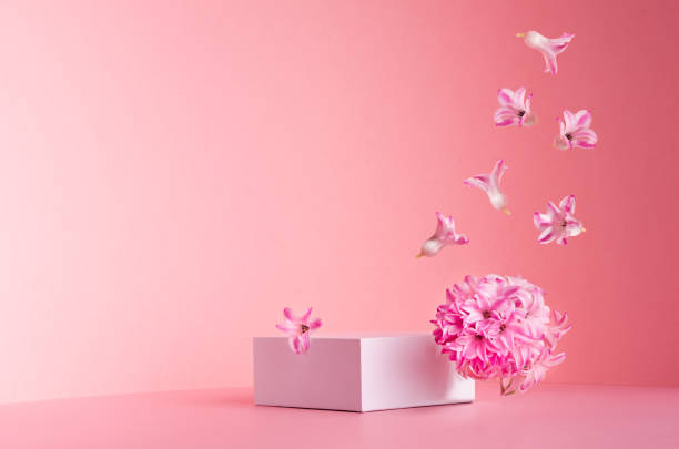 istock White square podium for display cosmetic and goods with hovering flow of fresh spring flowers  on gentle pastel pink background, copy space, modern fashion style. 1316780438