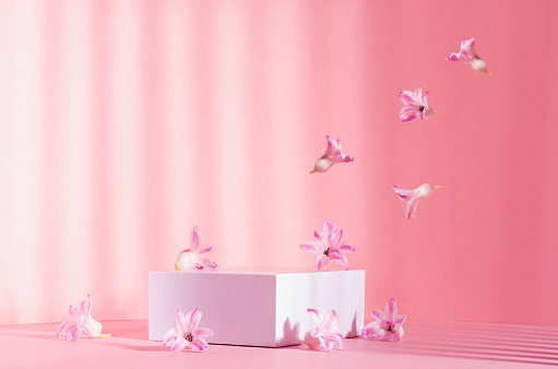 Romantic elegance three white square podiums with flow of levitate spring  flowers in sunlight with striped shadow on soft light pastel pink background. Fashion fresh showcase.