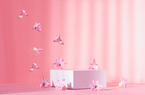 istock Bright spring mock up for cosmetic and product display with three white square podiums, stream of tender flowers flying in sun beam on pastel pink background. 1316780542