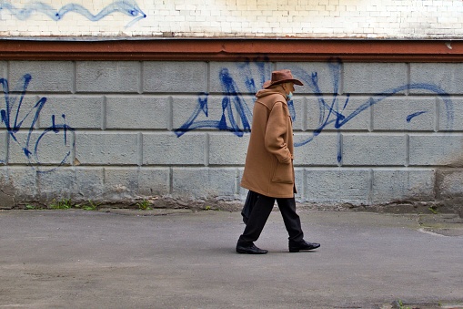 Lonely elderly man in wide brimmed hat and disposable face mask walks along a deserted street. Ukraine Zhytomyr May 07 2021