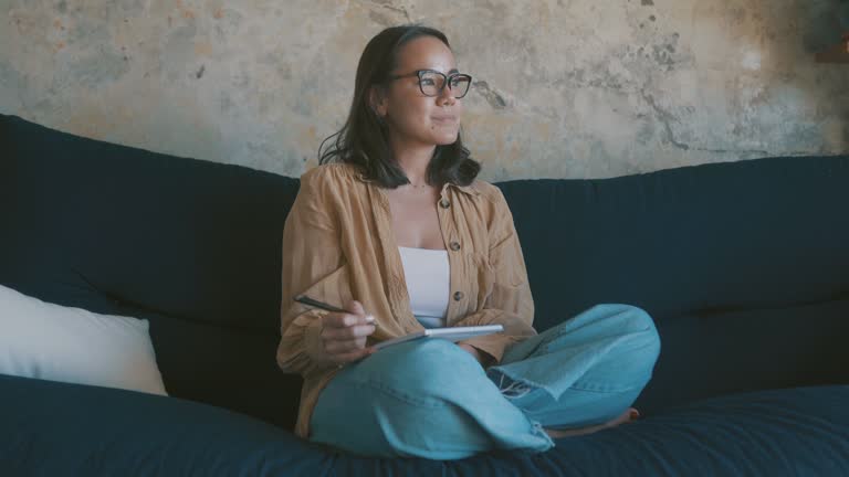 4k video footage of a young woman writing in her book on the couch at home