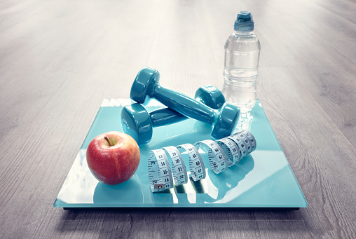 Fitness dumbbells, bathroom scales, apple and tape measure in gym, diet concept