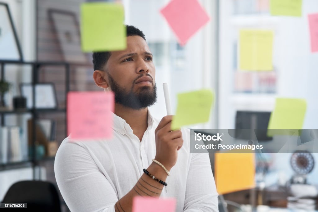Shot of a young businessman brainstorming with sticky notes on a glass wall in an office Something's missing... I just have to figure it out Decisions Stock Photo