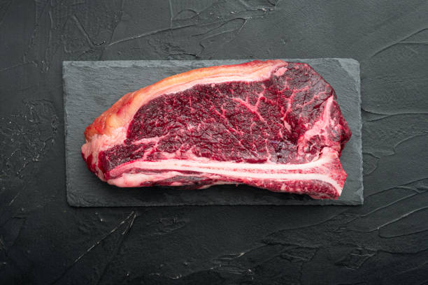 istock A raw fresh marbled beef steak, on black stone background, Club steak cut, top view flat lay, with copy space for text 1316787343