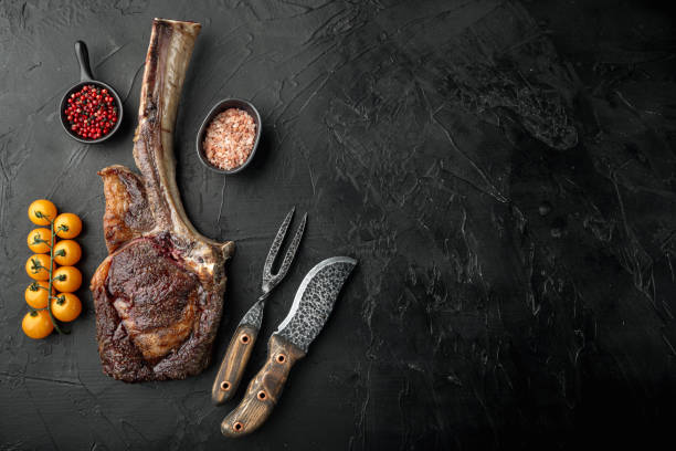 Grilled black angus beef tomahawk steak on bone, on black stone background, top view flat lay, with copy space for text