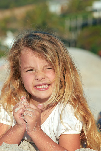 Cute little girl lying in the sand looking into the sun