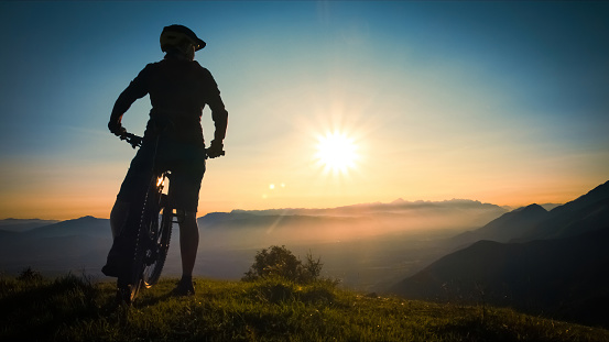 Back view of woman silhouette sitting on a mountain bike, enjoying an amazing view