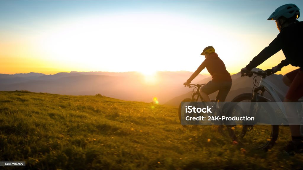 Cycling uphill with mountain bike Mother and daughter cycling uphill with mountain bikes at a sunset. Family Stock Photo