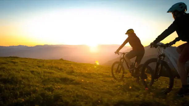 Mother and daughter cycling uphill with mountain bikes at a sunset.