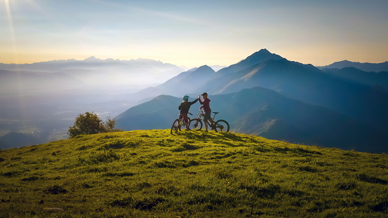 Two happy woman high five over the sunset after a successful mountain biking trip in the mountains. Celebrate a cross country cycling journey.