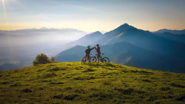 Photo of Woman high five over the sunset at mountain biking trip