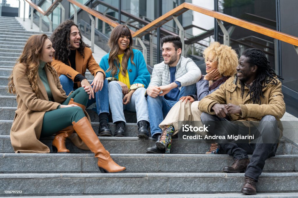 group of smiling young adults on a flight of steps, multiethnic friends having fun and laughing, resumption of sociality and safety after the pandemic, vaccinated people gathering Crowd of People Stock Photo